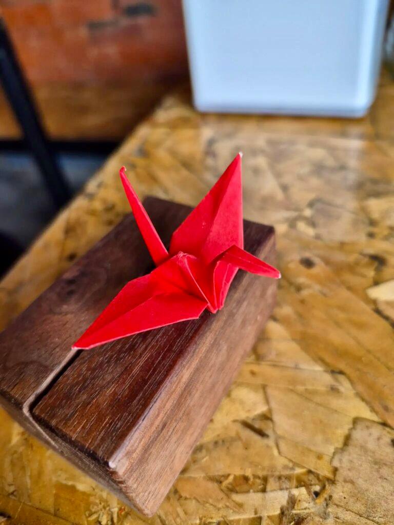 A red origami paper crane decoration placed on a wooden block at Rioba 901 restaurant.